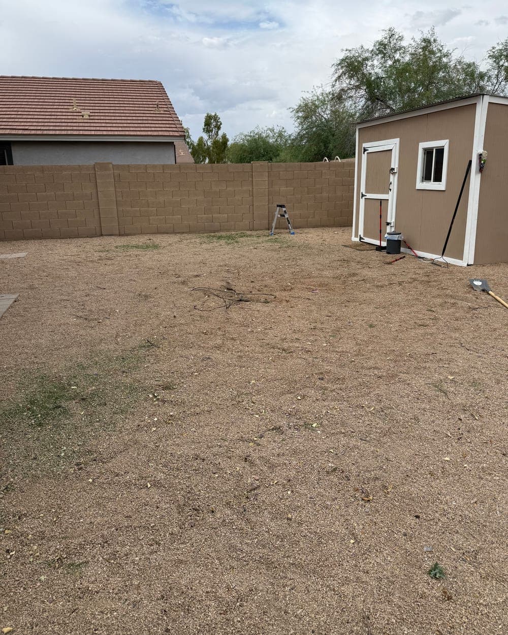 After: the same backyard cleared to bare gravel, the shed and block wall clear