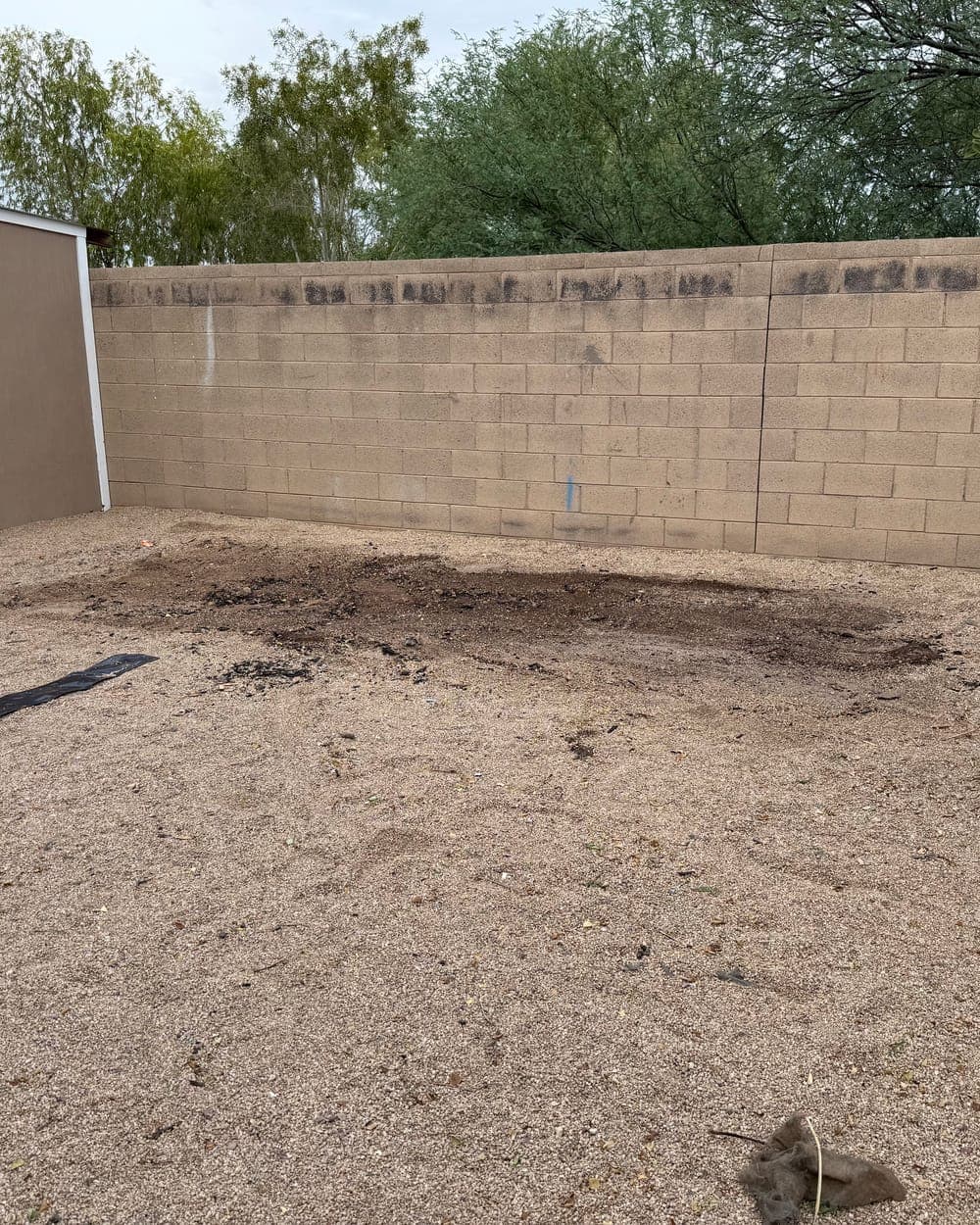 After: the swing set gone, only a dark patch of soil left on the gravel by the wall