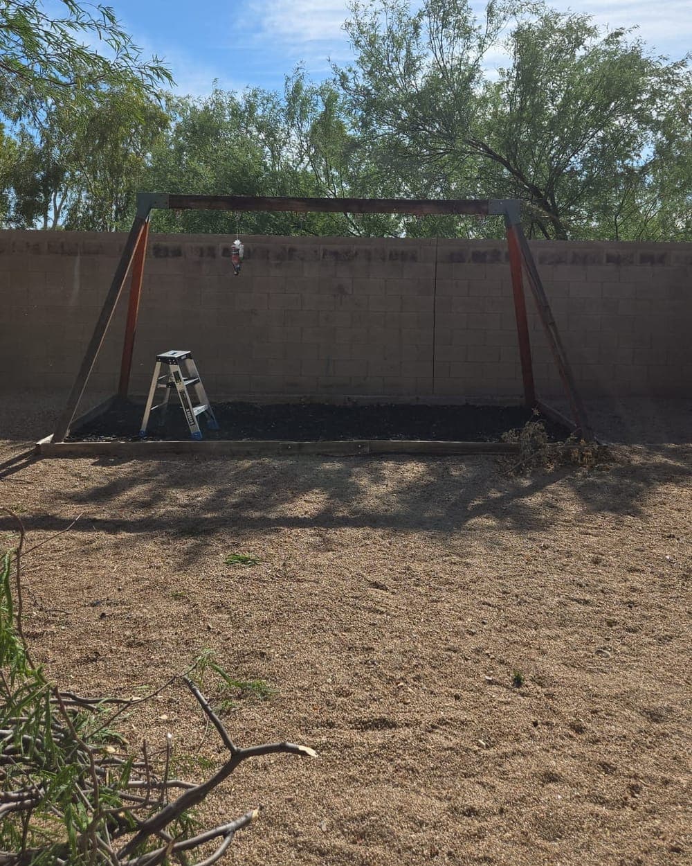 Before: an old wooden swing set frame standing against a block wall in a backyard